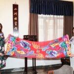 The President's wife (left) takes a photo with a long scarf of double dragons playing with pearls in her hand