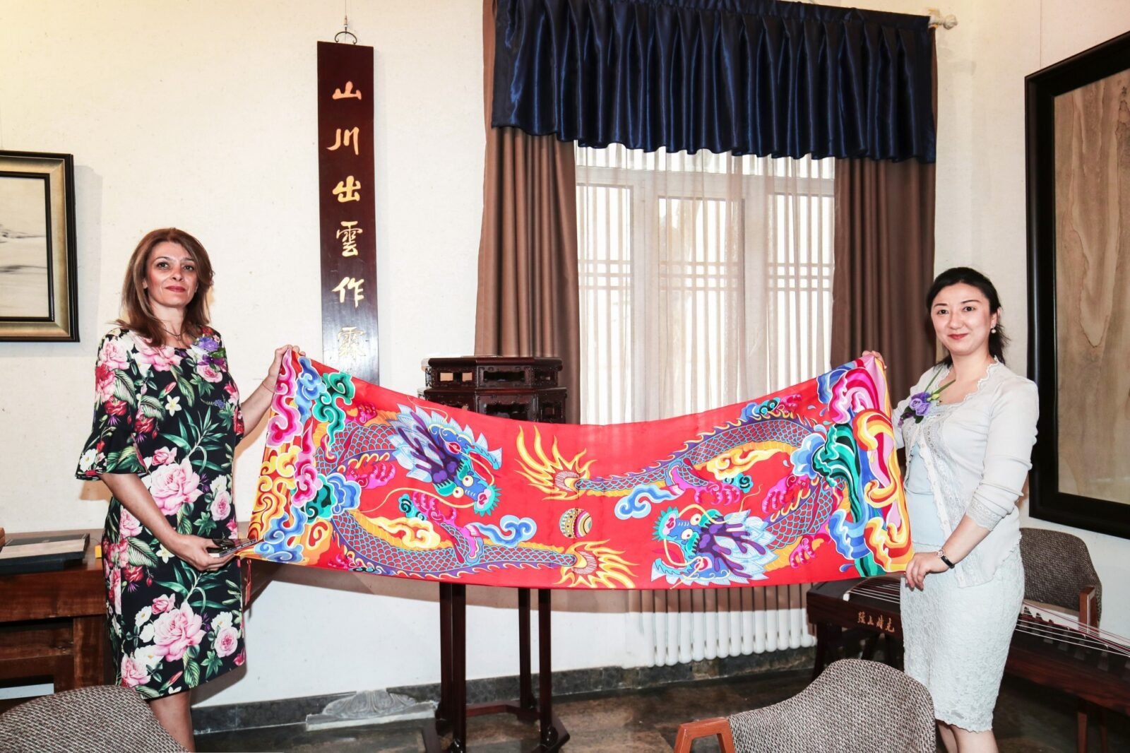 The President's wife (left) takes a photo with a long scarf of double dragons playing with pearls in her hand